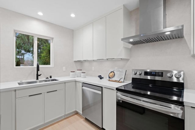 kitchen featuring appliances with stainless steel finishes, white cabinetry, sink, light hardwood / wood-style floors, and wall chimney exhaust hood