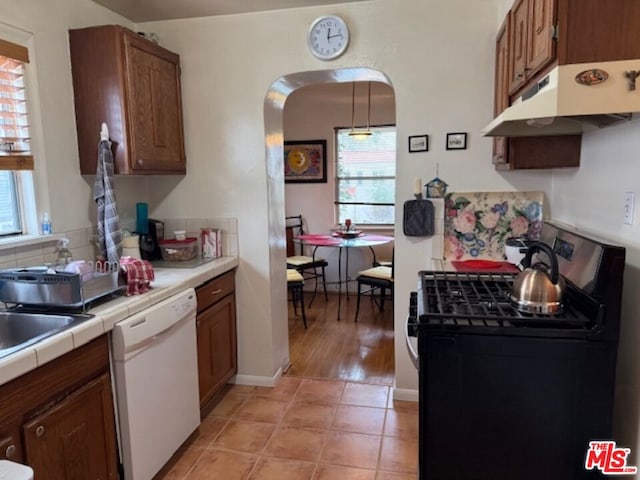 kitchen featuring light tile patterned flooring, gas stove, tile counters, dishwasher, and pendant lighting