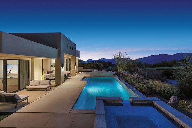 pool at dusk featuring an in ground hot tub, a mountain view, and a patio area