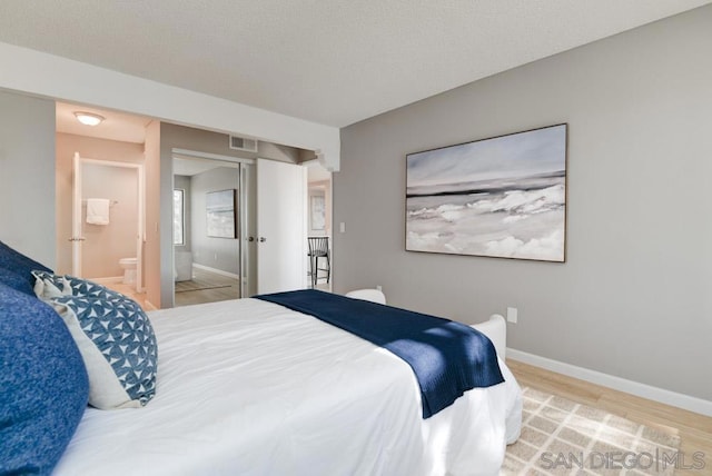 bedroom featuring light hardwood / wood-style flooring, a textured ceiling, and ensuite bathroom