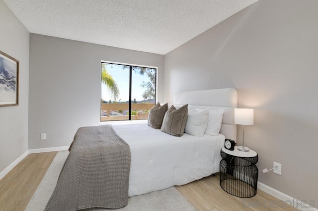 bedroom featuring wood-type flooring, access to exterior, and a textured ceiling