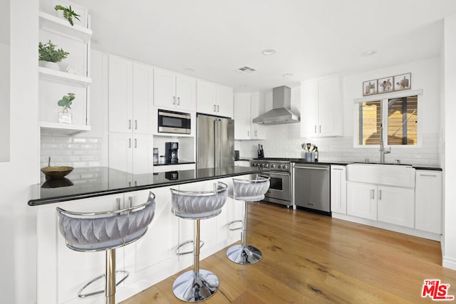 kitchen featuring white cabinetry, sink, a breakfast bar area, premium appliances, and wall chimney exhaust hood