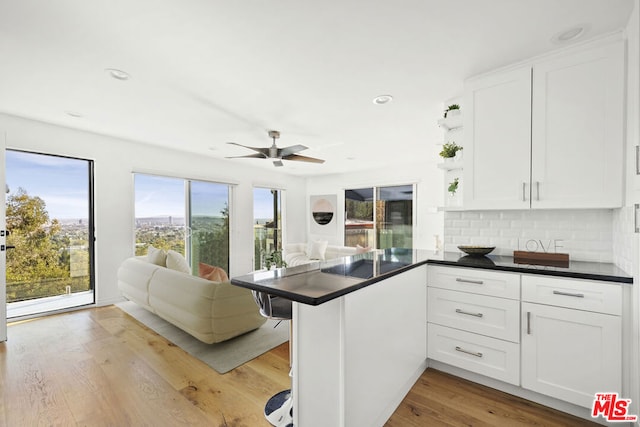 kitchen featuring tasteful backsplash, white cabinetry, light hardwood / wood-style floors, and kitchen peninsula