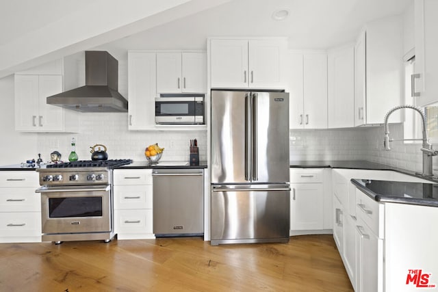 kitchen featuring sink, white cabinetry, premium appliances, light hardwood / wood-style floors, and wall chimney range hood