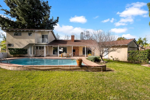 rear view of property with a balcony, a patio area, and a lawn