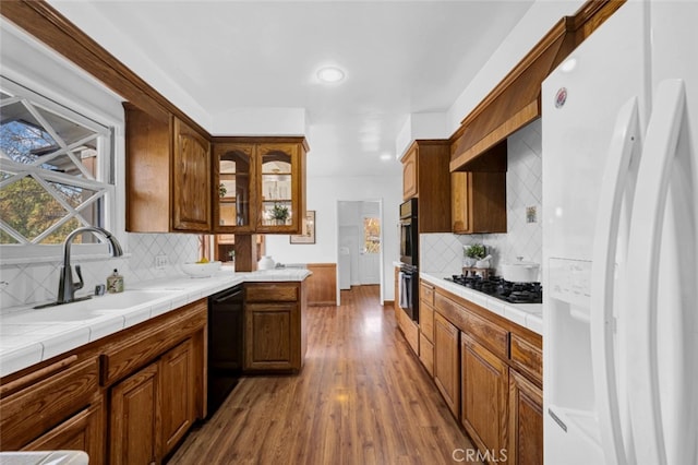 kitchen featuring tile countertops, wood-type flooring, sink, decorative backsplash, and black appliances