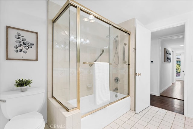 bathroom with toilet, tile patterned floors, and bath / shower combo with glass door