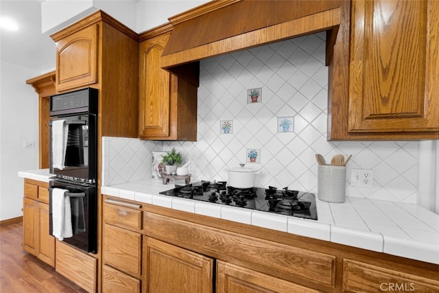 kitchen with tile countertops, double oven, light hardwood / wood-style flooring, and gas stovetop