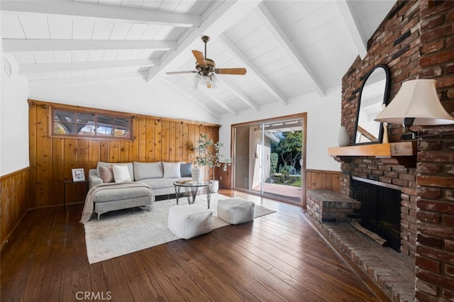 living room with vaulted ceiling with beams, dark hardwood / wood-style floors, wooden walls, ceiling fan, and a fireplace