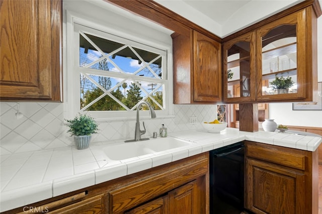 kitchen featuring black dishwasher, sink, tile counters, and backsplash