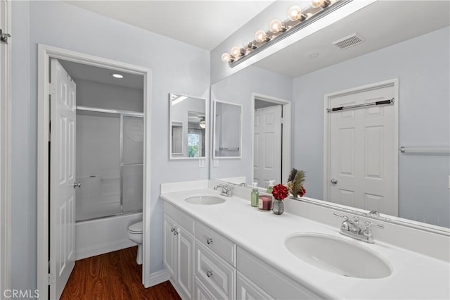 full bathroom featuring hardwood / wood-style flooring, enclosed tub / shower combo, vanity, and toilet