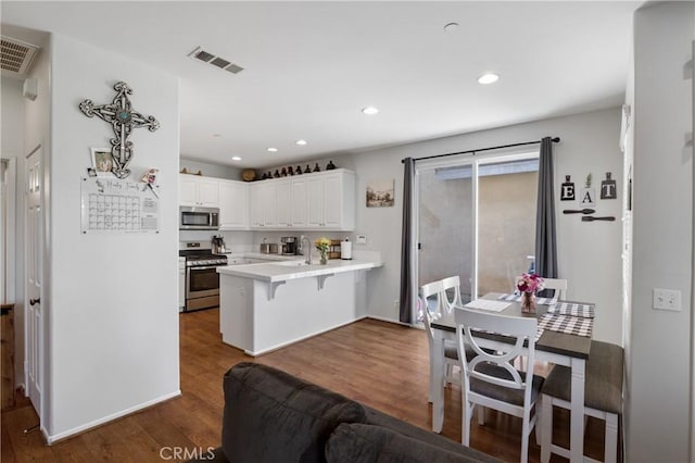 kitchen with dark hardwood / wood-style floors, a breakfast bar area, white cabinets, kitchen peninsula, and stainless steel appliances