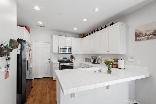 kitchen featuring white cabinetry, tile countertops, appliances with stainless steel finishes, dark hardwood / wood-style flooring, and kitchen peninsula