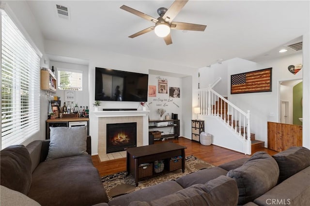 living room with ceiling fan, wood-type flooring, and a tiled fireplace