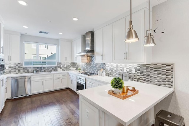 kitchen featuring pendant lighting, sink, stainless steel appliances, white cabinets, and wall chimney exhaust hood