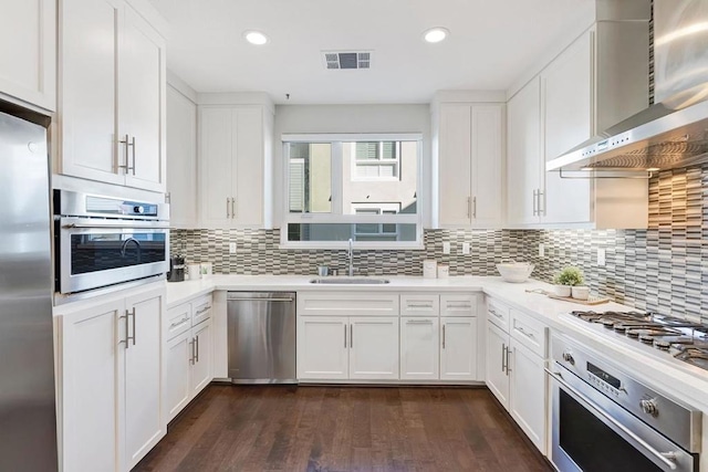 kitchen with wall chimney range hood, sink, stainless steel appliances, tasteful backsplash, and white cabinets