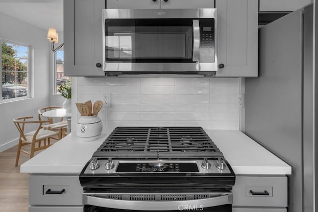 kitchen featuring decorative backsplash, gray cabinets, light hardwood / wood-style floors, and appliances with stainless steel finishes