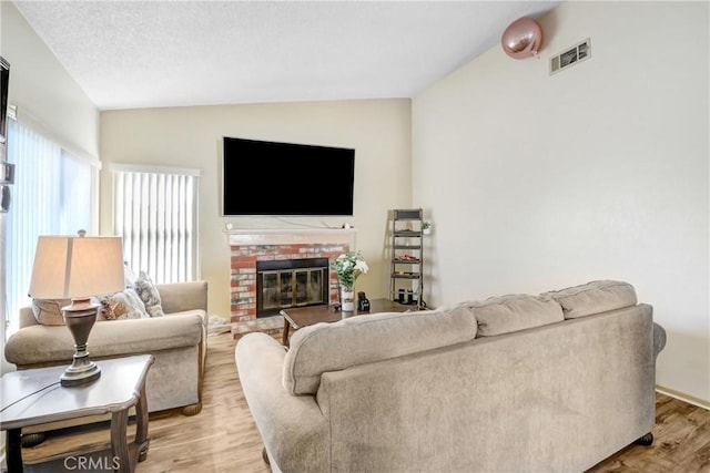 living room featuring lofted ceiling, a fireplace, light hardwood / wood-style floors, and a textured ceiling