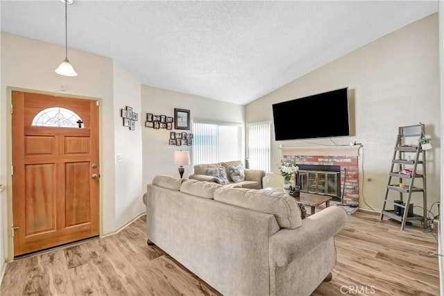 living room featuring lofted ceiling, a brick fireplace, light hardwood / wood-style flooring, and a textured ceiling