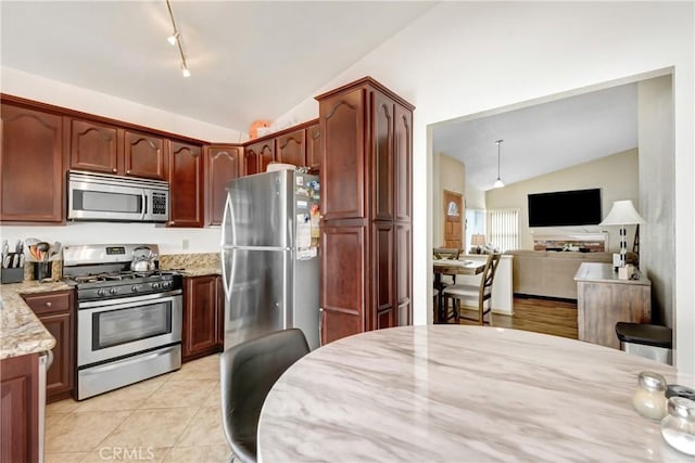 kitchen with light stone countertops, light tile patterned floors, vaulted ceiling, and stainless steel appliances