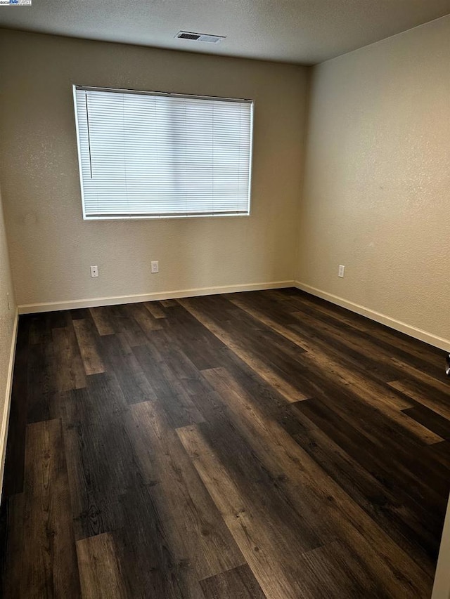 empty room with dark hardwood / wood-style flooring and a textured ceiling