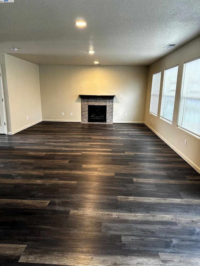 unfurnished living room with a tile fireplace, dark hardwood / wood-style floors, and a textured ceiling