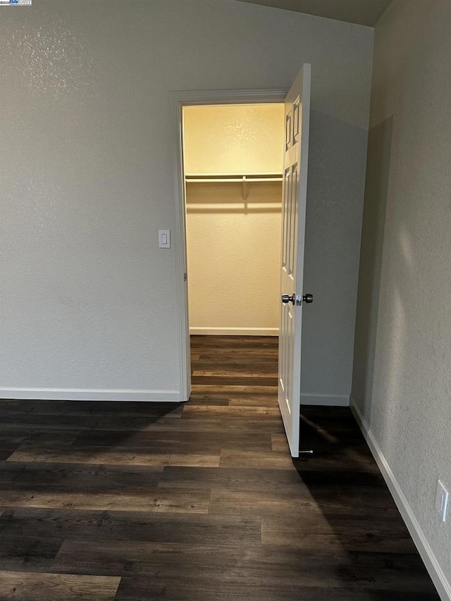 unfurnished bedroom featuring dark wood-type flooring, a spacious closet, and a closet