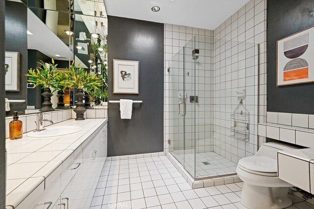 bathroom featuring a shower with shower door, tile walls, vanity, toilet, and tile patterned floors