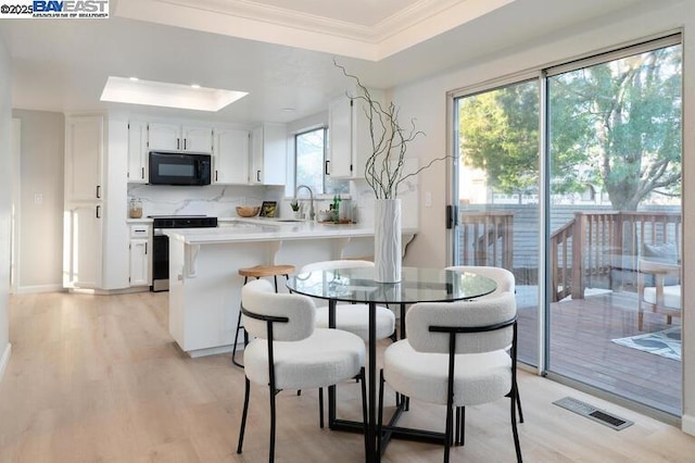 kitchen with kitchen peninsula, a skylight, white cabinets, stainless steel range with electric cooktop, and a tray ceiling