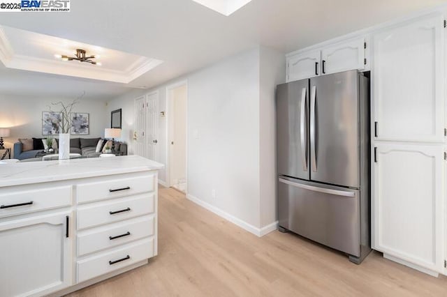 kitchen with white cabinetry, light wood-type flooring, stainless steel refrigerator, and a tray ceiling