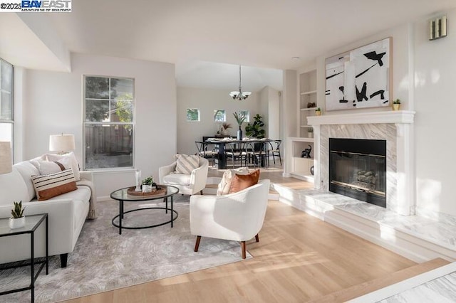 living room with built in shelves, a fireplace, an inviting chandelier, and hardwood / wood-style flooring