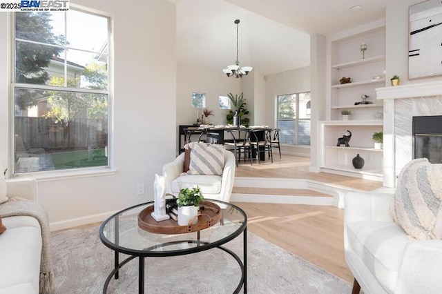 living room with a high end fireplace, built in features, a chandelier, and light wood-type flooring