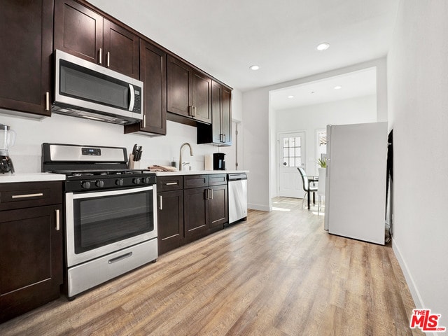 kitchen featuring appliances with stainless steel finishes, sink, dark brown cabinets, and light wood-type flooring