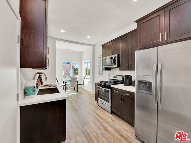 kitchen with dark brown cabinetry, sink, stainless steel appliances, and light wood-type flooring