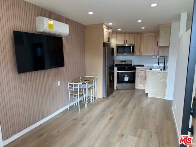 kitchen with appliances with stainless steel finishes, an AC wall unit, light brown cabinetry, sink, and light wood-type flooring