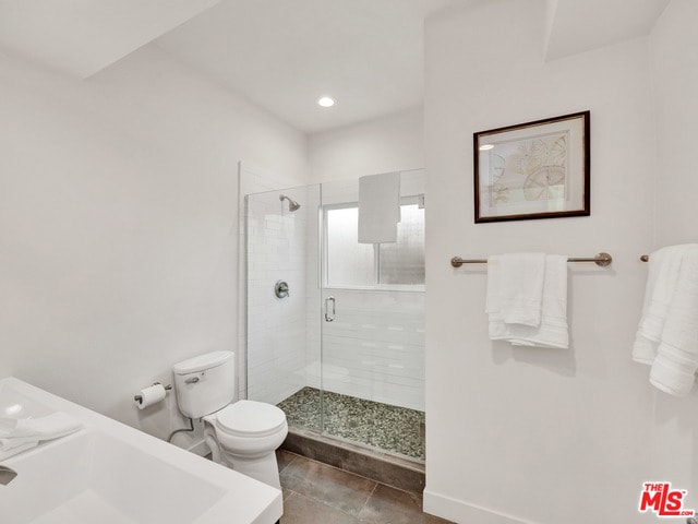 bathroom featuring tile patterned flooring, a shower with shower door, and toilet