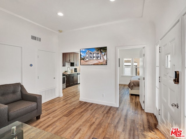 living room featuring crown molding, sink, and light hardwood / wood-style floors