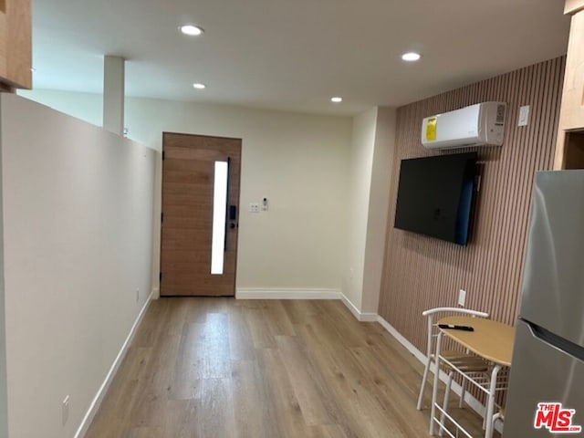 foyer entrance with a wall mounted air conditioner and light hardwood / wood-style flooring