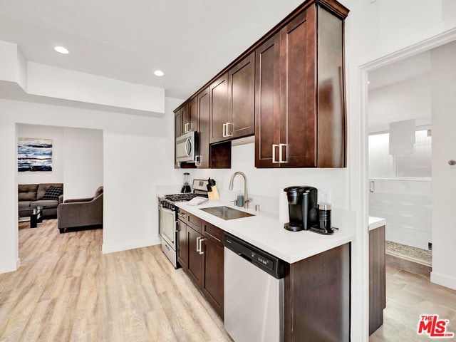 kitchen with appliances with stainless steel finishes, sink, dark brown cabinets, and light wood-type flooring