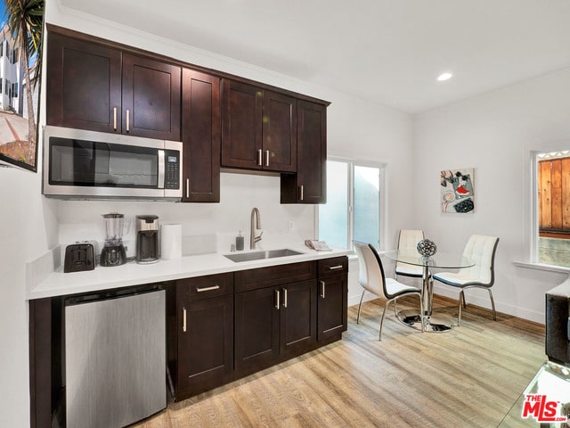 kitchen with stainless steel appliances, sink, dark brown cabinetry, and light wood-type flooring