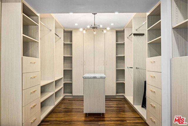 spacious closet with an inviting chandelier and dark wood-type flooring