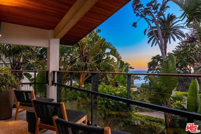 balcony at dusk featuring a water view