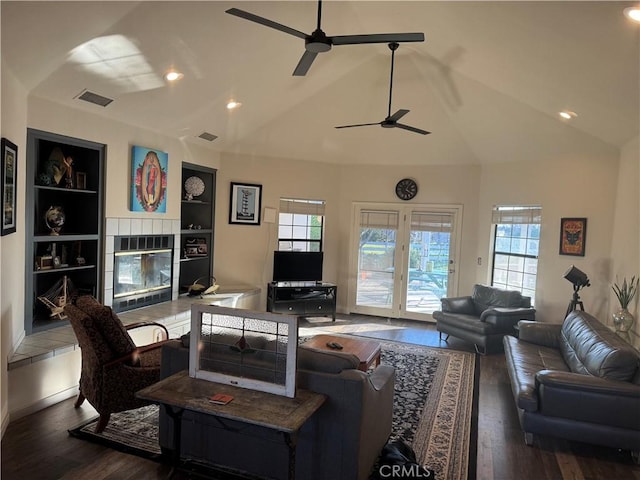 living area featuring lofted ceiling, built in shelves, a tile fireplace, wood finished floors, and visible vents