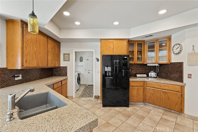 kitchen featuring black refrigerator with ice dispenser, a sink, washer / dryer, brown cabinetry, and recessed lighting