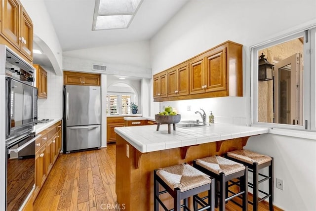 kitchen with sink, tile counters, stainless steel fridge, and a kitchen breakfast bar