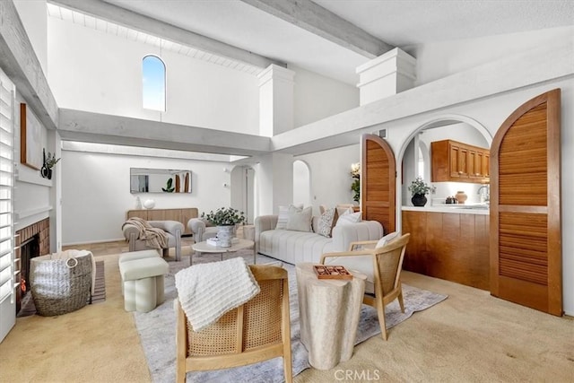 carpeted living room featuring a fireplace, high vaulted ceiling, and beam ceiling