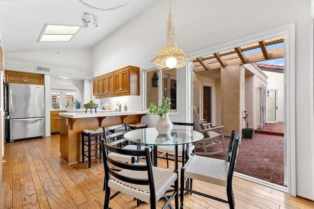 dining space with high vaulted ceiling, a skylight, and light hardwood / wood-style floors