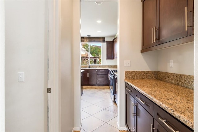 kitchen featuring dark brown cabinetry, sink, stainless steel gas range oven, light tile patterned floors, and light stone countertops