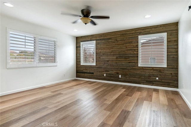 spare room with ceiling fan, light hardwood / wood-style floors, and wood walls