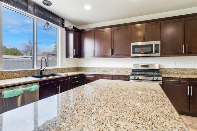 kitchen featuring dark brown cabinetry, sink, hanging light fixtures, stainless steel appliances, and light stone countertops